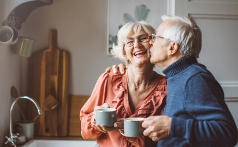 Mature couple happily embracing in kitchen, holding coffee cups