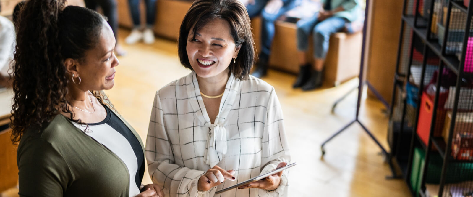 Two women smiling at each other while using a tablet device