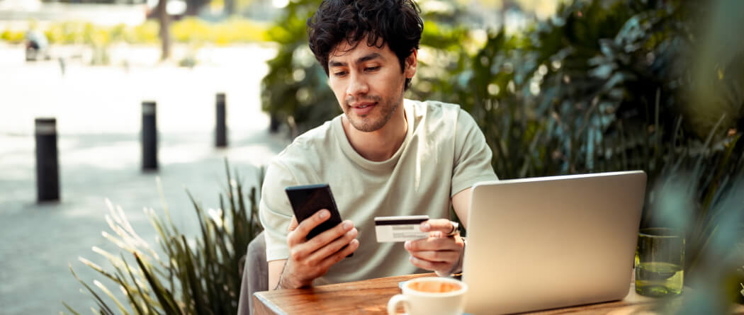 Man holding credit/debit card and mobile phone at an outdoor cafe