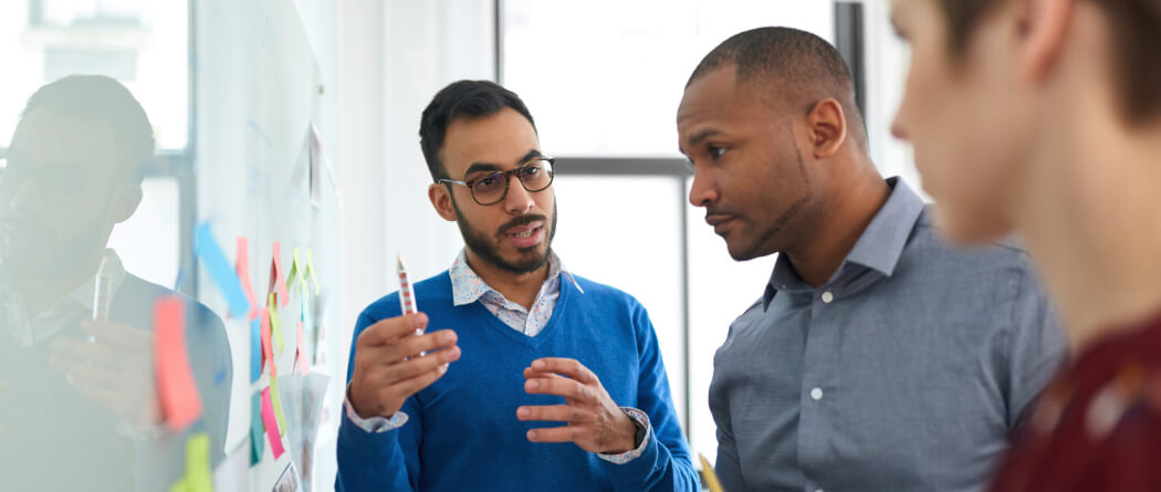 Group of three people brainstorming at a white board with sticky notes